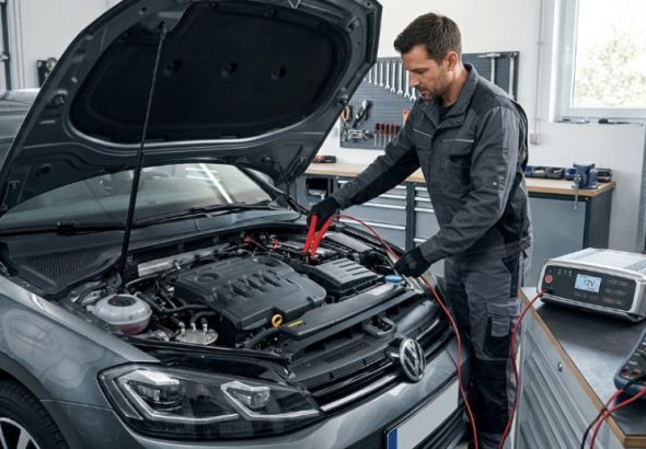 Автомеханік підключає зарядний пристрій до акумулятора авто.
